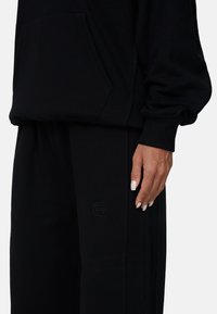 Zwart sweatshirt en sweatpants set. Zacht materiaal, ontspannen pasvorm. Voorzien van een voorzak, ribgebreide boorden en een reliëflogo op de broek.