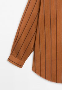 Long sleeve of a brown shirt with vertical black stripes and a wide cuff folded at the wrist.