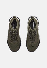 Zielone tekstylne buty do wędrówek z czarnymi gumowymi podeszwami, z okrągłymi sznurowadłami, perforowanymi sekcjami oraz białym akcentem wzdłuż śródpodeszwy.