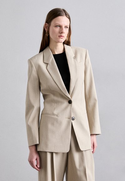 Blazer bej croit cu umăr, închidere cu un singur nasture și două buzunare frontale. Material texturat, rever ascuțit și croială supradimensionată.