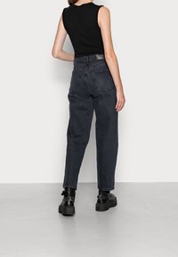 Vaqueros negros de talle alto con un ajuste relajado, hechos de mezclilla. Presentan un ligero desgaste, bolsillos traseros y una etiqueta de cuero en la cinturilla.