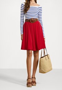 Jupe rouge trapèze associée à un chemisier à manches longues rayé bleu et blanc, ceinture tressée marron et sandales à plateforme marron. Sac cabas en paille tissée.