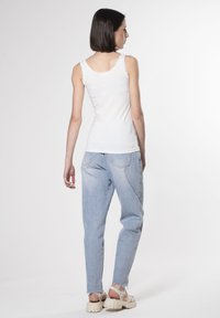 Weißes Baumwoll-Top mit Spitze, kombiniert mit hellblauen, schmal zulaufenden Jeans. Die Jeans weisen eine leicht ausgewaschene Textur und einen rohen Saum auf.