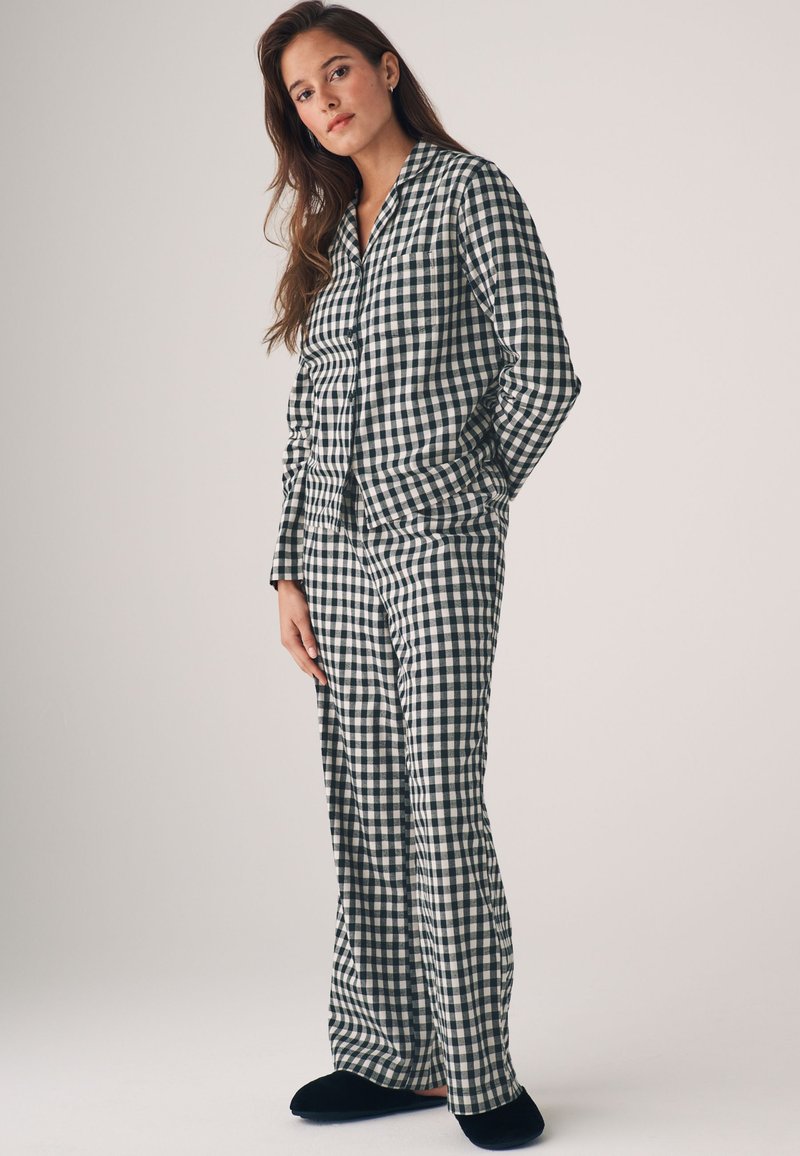 Kockás pizsama szett sötétkék és fehér színben, galléros gombos inggel és széles lábú nadrággal. Puha anyag, laza szabás. Fekete papucs.