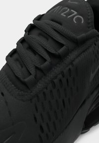 Gros plan d'une chaussure de sport noire avec une tige en mesh texturé, des lacets épais et « AIR270 » imprimé sur la languette rembourrée.
