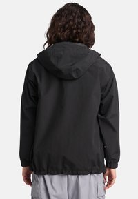Svart huva jacka gjord av lätt material, med elastiska mudd och dragsko i nederkant, med en slät textur och minimalistisk design.