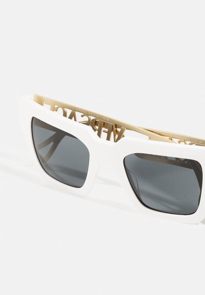 Occhiali da sole bianchi oversize con lenti grigie rettangolari, dotati di un dettaglio in metallo dorato con logo all'interno della montatura.