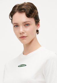 Hvid T-shirt med rund halsudskæring, prydet med et grønt "RIPE & FRESH" logo. Stoffet ser glat ud med en standard pasform.
