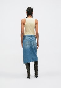 Μπεζ αμάνικο τοπ συνδυασμένο με μπλε τζιν φούστα μίντι, με δύο πίσω τσέπες και ξεφτισμένο τελείωμα, συμπληρωμένο με μαύρες μπότες μέχρι το γόνατο.