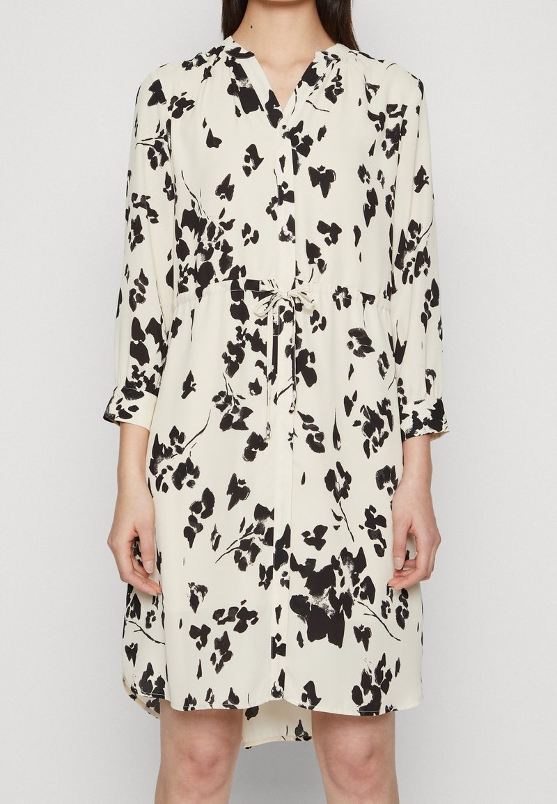 Kukkaistulostusmekko kerma-valkoisella pohjalla, mustilla kuvioilla, pitkät hihat, V-pääntie ja vyötärösolki. Pehmeä kangas, rento istuvuus ja pyöristetty helma.