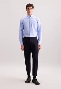 Hellblaues Hemd mit Knöpfen und Tasche, kombiniert mit dunkler, maßgeschneiderter Hose und schwarzen Lederschuhen. Glatter Stoff und strukturierte Passform.