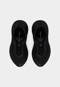 Μαύρα αθλητικά παπούτσια Calvin Klein με στρογγυλεμένη μύτη, σχεδιασμό slip-on, ελαστικά κορδόνια και λογότυπο "cK" στη γλώσσα, σε άποψη από πάνω σε λευκό φόντο.