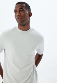Lys grå T-shirt med korte ærmer, rund halsudskæring og glat tekstur. Har subtile sømme og en afslappet pasform.