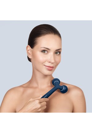 Vrouw met bruin haar gebruikt een blauwe handmassage op haar schouder tegen een effen lichtblauwe achtergrond.