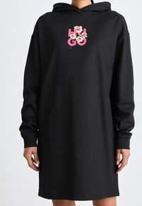 Vestido sudadera negro hecho de una tela suave y lisa. Cuenta con capucha, mangas largas y un logotipo floral en la parte frontal en rosa y blanco.