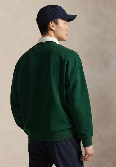 Πράσινο φούτερ από μαλακό ύφασμα με άνετη εφαρμογή. Διαθέτει ριμπ γιακά και μανσέτες, συνδυασμένο με σκούρο μπλε παντελόνι.