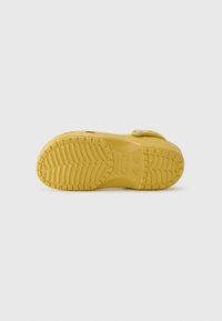 Yellow rubber shoe sole with textured grip pattern, featuring a rounded shape and a circular logo detail. Includes a side strap for secure fit.