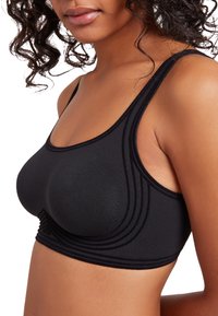 Soutien-gorge de sport noir avec une texture lisse, des bretelles larges et des détails de couture horizontale ; offre un ajustement confortable et une silhouette frontale arrondie.