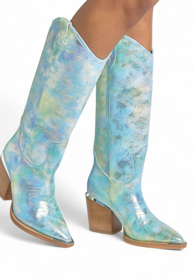 Botas hasta la rodilla en color turquesa con textura brillante, acentos metálicos, puntera afilada, tacón apilado y patrones de costura decorativos.