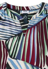 Col et partie supérieure de la poitrine d'une chemise à motifs multicolores avec un décolleté en V et des étiquettes de marque indiquant CECIL et BE KIND.