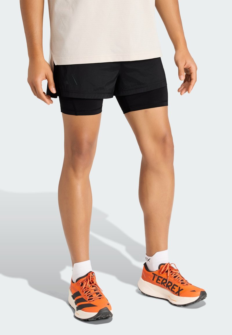 Musta urheilushortsit, joissa on sisäinen vuori, yhdistettynä kirkkaan oransseihin juoksukenkiin, joissa on mustia yksityiskohtia, ja valkoisiin sukkiin.