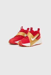 Κόκκινα αθλητικά παπούτσια με χρυσό ιμάντα στη μέση του ποδιού, λευκό λογότυπο, πλεκτό επάνω μέρος, υφασμένο πέλμα και επενδυμένο κολάρο. Διαθέτουν έντονη αντίθεση χρωμάτων.