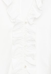 White blouse featuring a deep V-neckline, frilled detailing along the front, and six button closures, made of lightweight fabric.