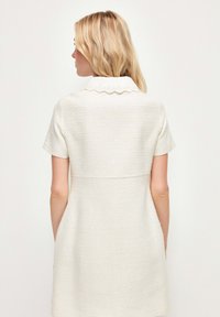 Vestido blanco de manga corta hecho de tejido texturizado. Presenta un cuello con puntas y un cuerpo ajustado que se estrecha hacia el dobladillo.