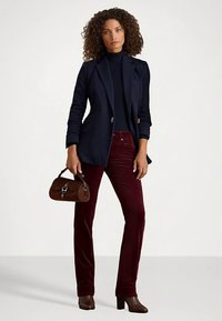 Marineblå blazer, ribbestrikket rullekragegenser, burgunderrøde kordfløyelbukser, brun håndveske og brune støvletter med hæl. Krøllete hår som rammer inn ansiktet.