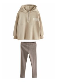 Beige hoodie med dragkedja och framtryckt lettering, kombinerad med ruggade bruna leggings. Mjuk bomullsmaterial, avslappnad passform och minimal design.