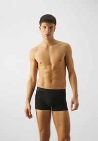 Schwarze Baumwoll-Boxershorts mit elastischem Bund, taillierter Passform und glatter Textur, getragen von einem Model vor einem einfarbigen Hintergrund.