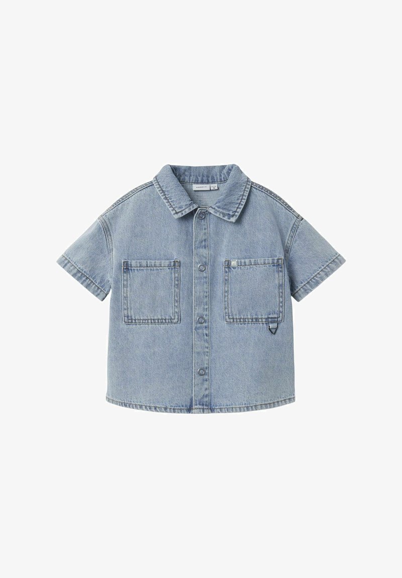 Camisa de mezclilla de manga corta en azul claro, con cuello puntiagudo, dos bolsillos frontales y cierre de botones en la parte delantera con costuras en contraste.