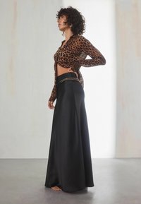 Košile s leopardím vzorem a dlouhým rukávem, uvázaná v pase, ve spojení s černou saténovou maxi sukňou se zdobeným pasem a volným siluetou.