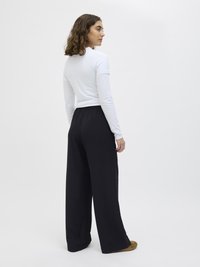 Un haut blanc à manches longues associé à un pantalon noir à jambes larges. La tenue présente un design ajusté et une texture lisse, sans motifs visibles.