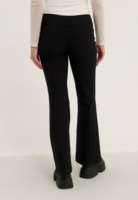 Black flared pants with a soft texture, high waistband, and a smooth finish; paired with chunky black platform boots.