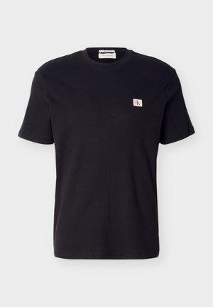 Black short-sleeve ribbed T-shirt with crew neck and small white patch logo on the left chest.