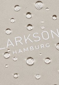 Il tessuto idrorepellente beige presenta una superficie testurizzata con gocce d'acqua. Il nome del marchio "CLARKSON HAMBURG" è stampato in bianco.