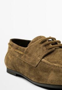 Brune ruskind loafers med rundet tå, syningsdetaljer og en glat gummisål. Har snørebånd og en subtil struktur i materialet.