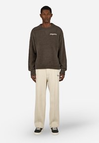 Temno siva puhasta jopica z logotipom na prsih, v kompletu s svetlo bež teksturiranimi hlačami in črnimi supergami z belimi vezalkami.