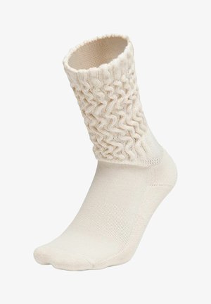 Cremefarbener Socken mit einem strukturierten, wellenförmigen Strickmuster am Bündchen und glattem Stoff am Fuß und Knöchel.