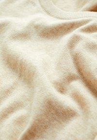 Béžová pletená látka s měkkou texturou, s žebrovaným límcem. Jemné barevné variace vytvářejí jemný, přirozený vzhled.