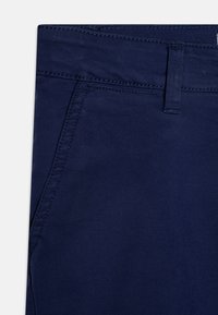 Pantalons en twill de coton bleu marine avec un devant plat, des poches latérales et des coutures visibles. Le matériau a une texture lisse.