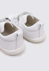 Chaussures en cuir blanc avec une finition lisse, bout rond et couture contrastante. Elles disposent d'une semelle en caoutchouc texturé et d'une boucle à l'arrière pour un enfilage facile.