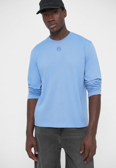 Svetlomodré tričko s dlhým rukávom a okrúhlym výstrihom, na hrudi s kruhovým logom. Materiál pôsobí mäkko a má hladkú textúru.