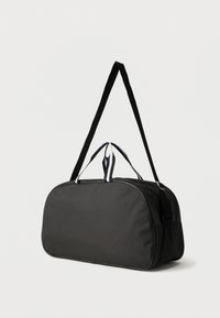 Μαύρη ορθογώνια τσάντα duffel με λευκά περιμετρικά χερούλια και ρυθμιζόμενο μακρύ λουρί ώμου, που στέκεται ενάντια σε ένα απλό λευκό φόντο.