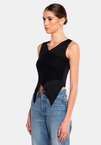 Svart ärmlös topp med en omslagdesign och spetsig kant, tillverkad av mjukt tyg. Kombinerad med ljusblå höga jeans.