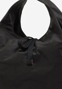 Czarna, błyszcząca torba nylonowa z zaokrąglonym otworem, z zamknięciem na sznurek i teksturowanym paskiem. Minimalistyczny design, brak widocznych wzorów czy metalowych elementów.