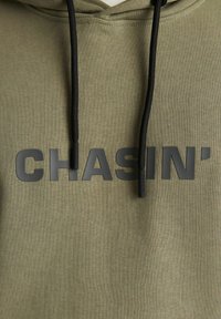 Olive green hoodie with black drawstrings, featuring bold, matte black print reading "CHASIN'" across the front. Textured fabric.
