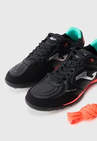 Black athletic shoes with leather and mesh materials, featuring a textured toe, silver accents, and a vibrant orange lace beside them.