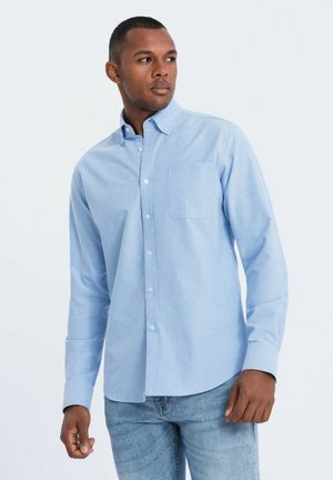 Light blue button-up shirt made of cotton blend, featuring a chest pocket, long sleeves, and a classic collar. Worn with blue jeans.
